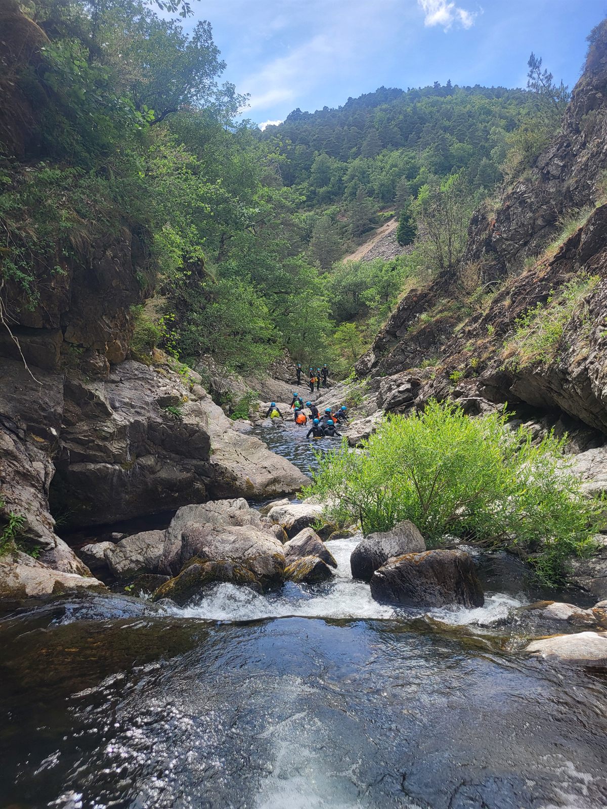 Groupe descendant le lit rocheux du canyon du Bramabiau, vallée verdoyante du mont Aigoual en arrière-plan, Cévennes